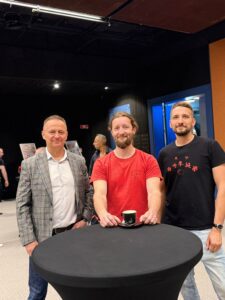 Trzech mężczyzn pozuje do zdjęcia przy czarnym stoliku podczas spotkania szkoły