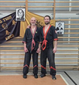 Dwóch instruktorów Wing Tsun w czarnych strojach z czerwonym wykończeniem przed drabinkami w sali gimnastycznej