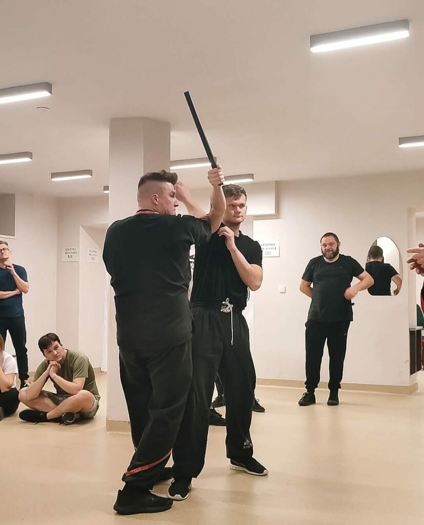 Szkolenie bezpieczeństwa dla szkół w Szczecinie Ćwiczenie z kijem podczas zajęć samoobrony w Szczecinie, uczestnicy w tle